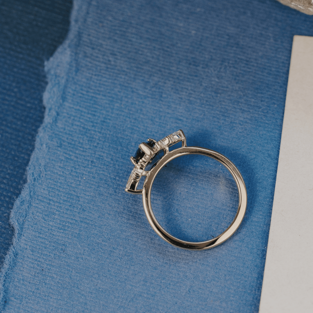 A 14k gold ring featuring a blue sapphire gemstone viewed from above, displayed on a textured blue surface.