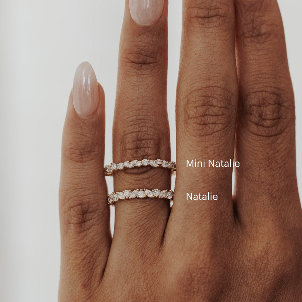 Hand wearing two diamond rings with 'Mini Natalie' and 'Natalie' branding on a neutral background.