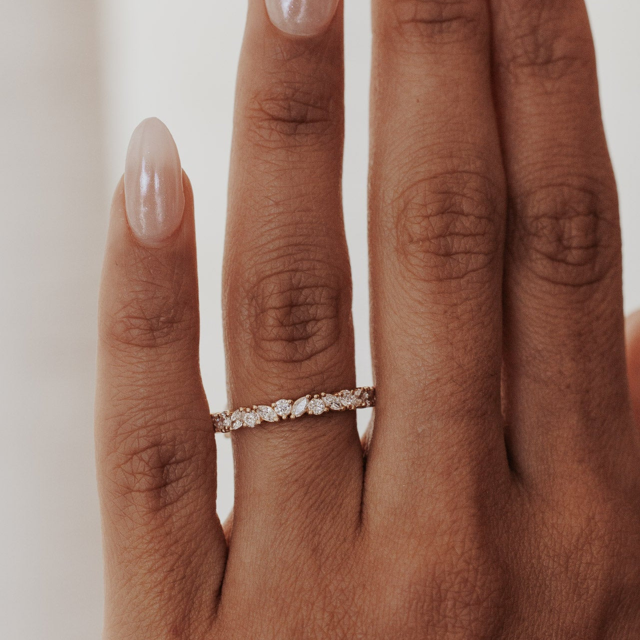 Close-up of a hand wearing a Natalie diamond wedding band on a neutral background.