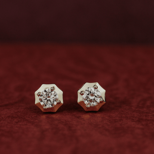14k gold diamond earrings set in prongs showcased on a textured red surface. 