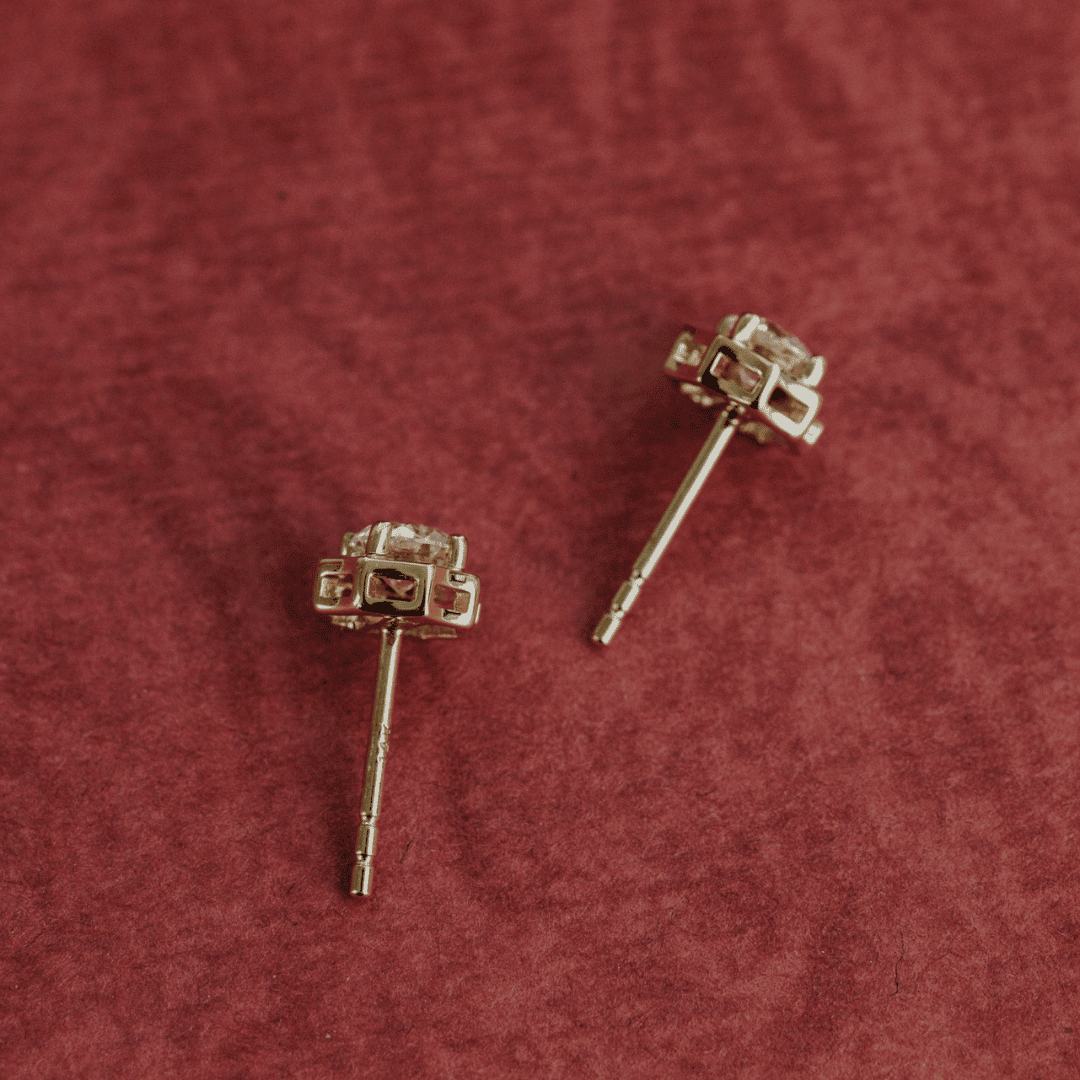 14k gold diamond earrings set in prongs showcased on a textured red surface at a side / top view. 