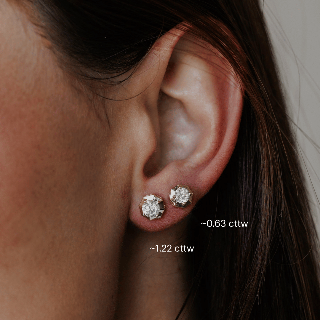 14k gold diamond earrings set in prongs showcased on the ear of a model. Both size carats are shown. 