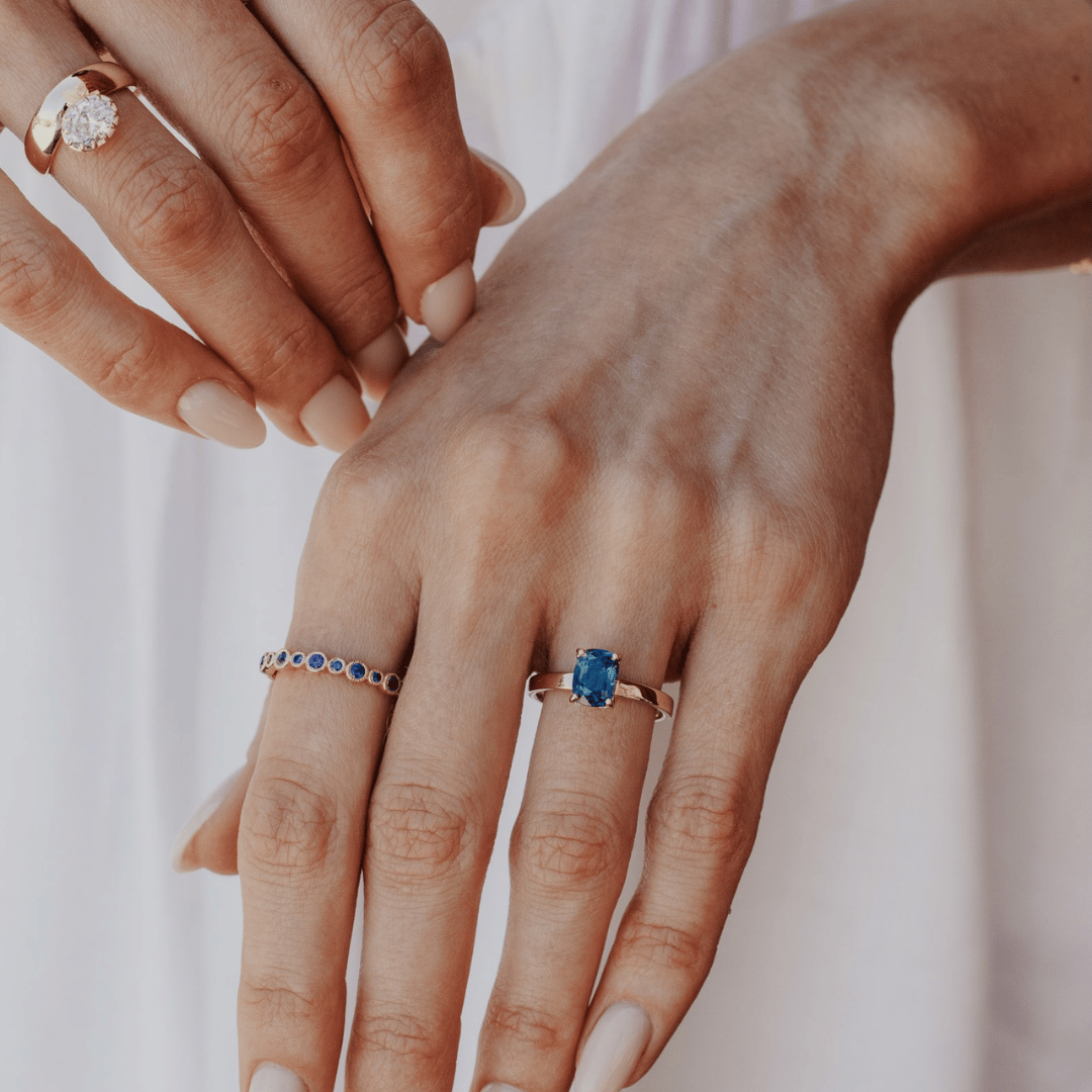 A 14k gold ring featuring a dark blue sapphire gemstone, displayed on the ring finger of a hand model. 