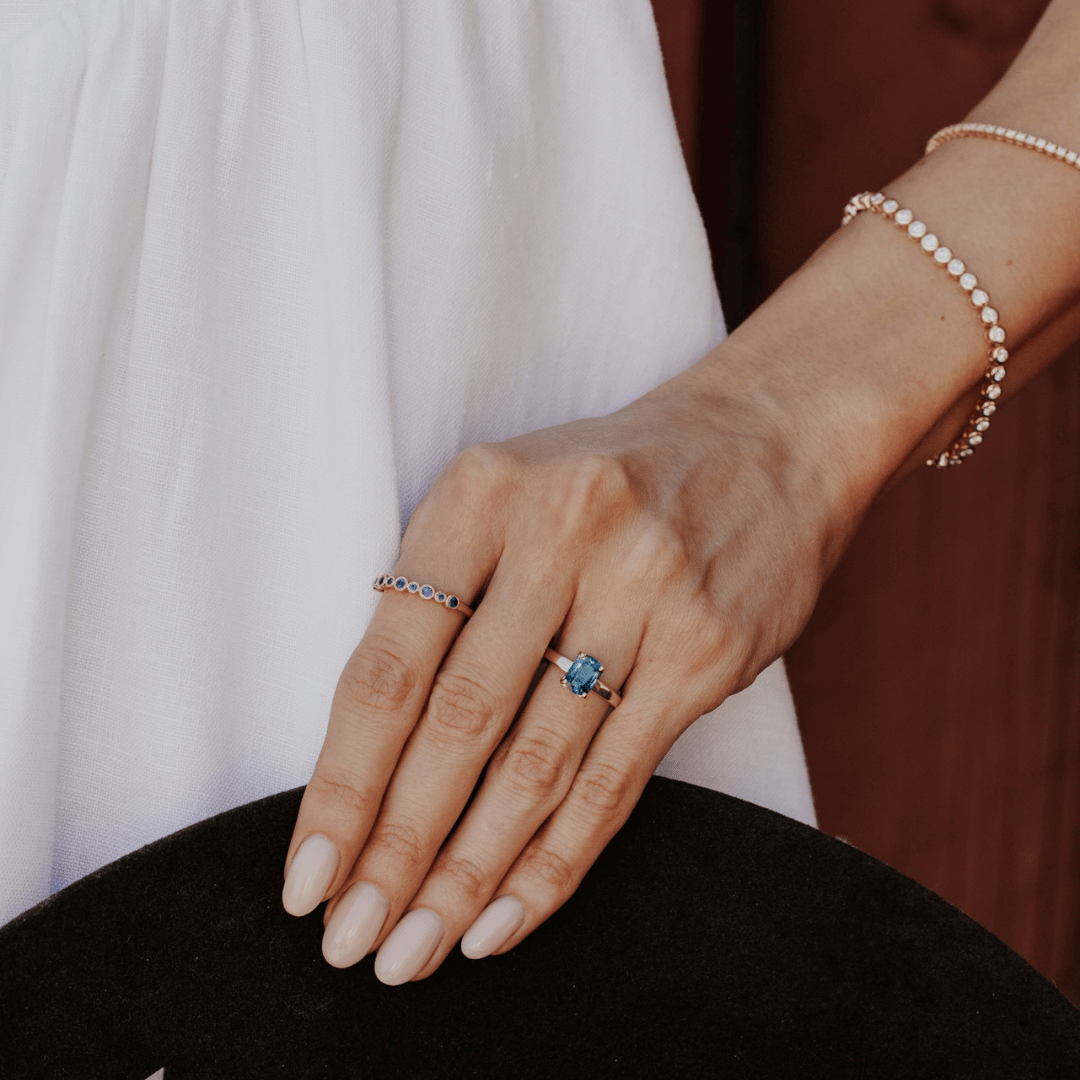 A 14k gold ring featuring a dark blue sapphire gemstone, displayed on the ring finger of a hand model. 
