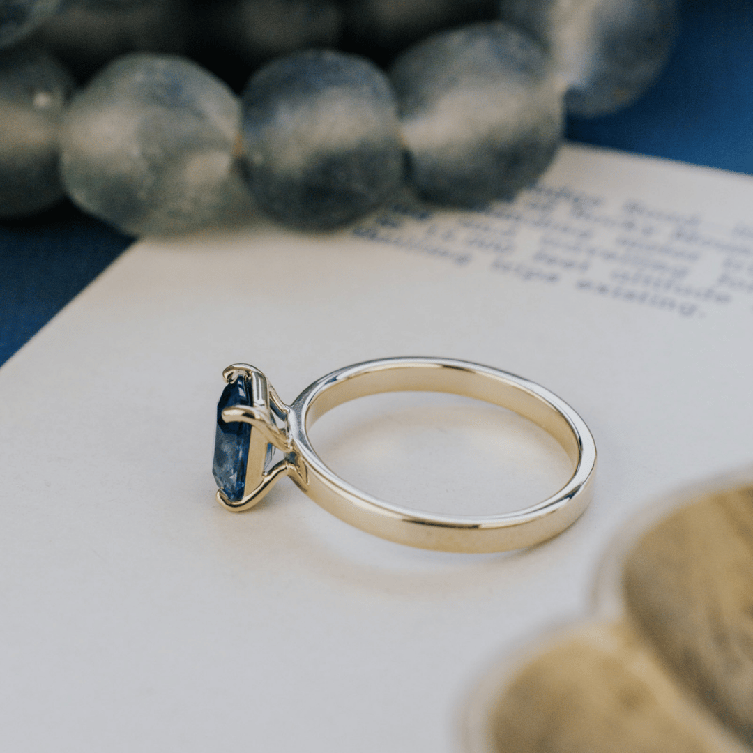 A 14k gold ring featuring a dark blue sapphire gemstone from, displayed on a textured white surface with a soft-focus background.the side view