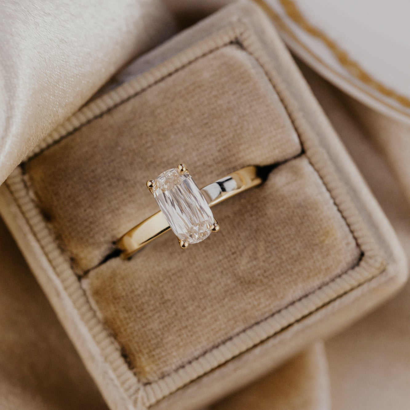 Gold Octavia ring with a champagne diamond in a beige jewelry box on a beige fabric background.