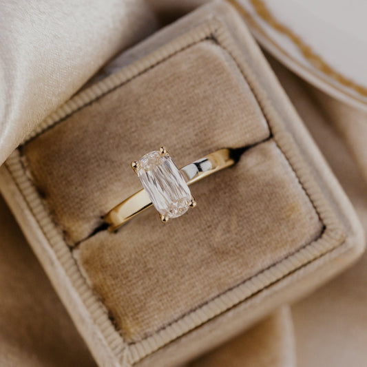 Gold Octavia ring with a champagne diamond in a beige jewelry box on a beige fabric background.