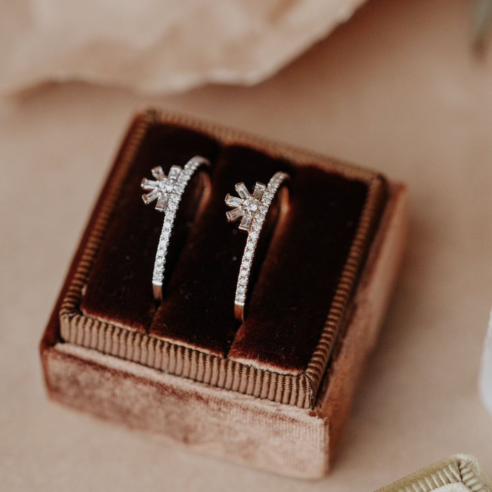 Two diamond wedding bands in a brown velvet box with a blurred flower in the background.