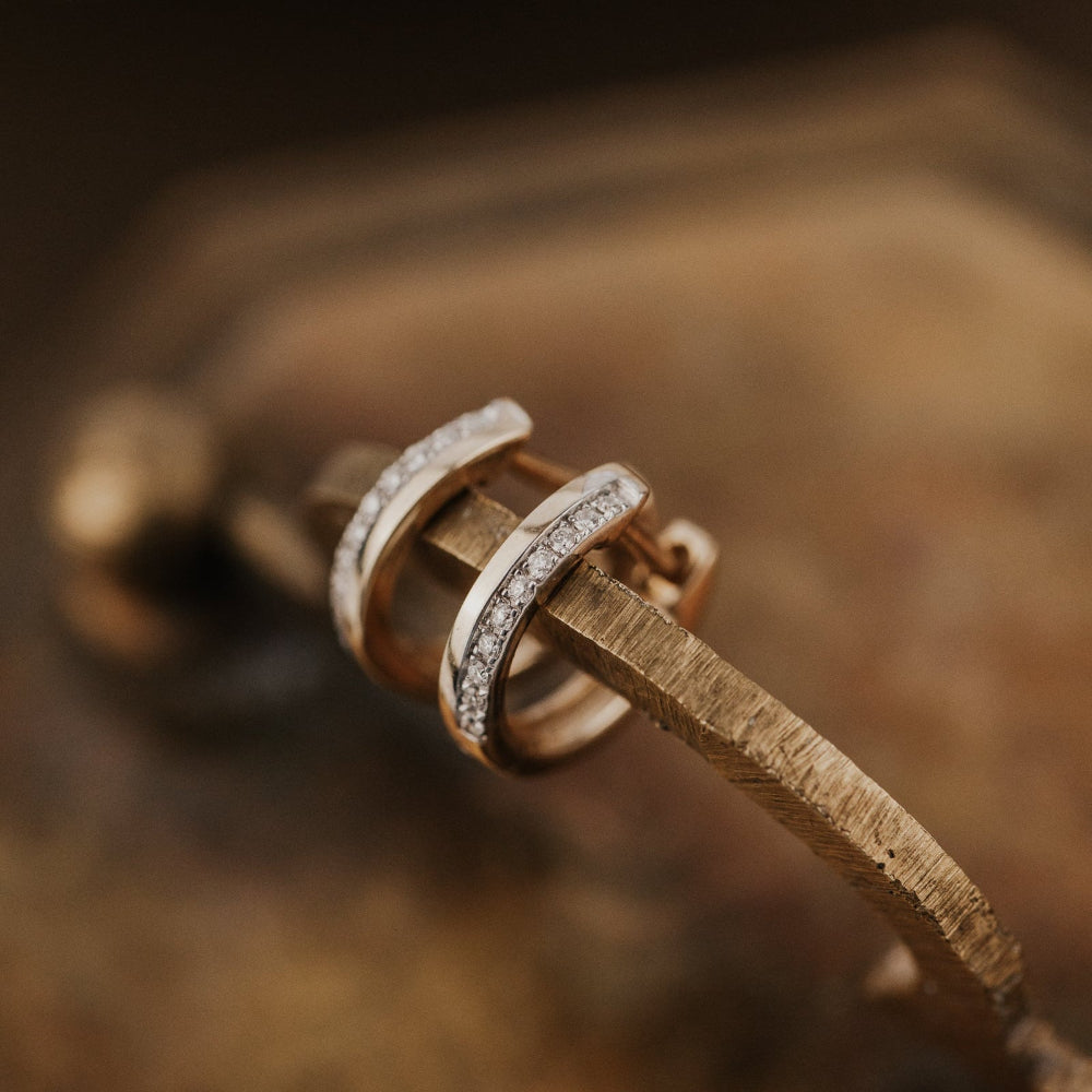 Close-up of gold earrings with diamond accents on a wooden surface.