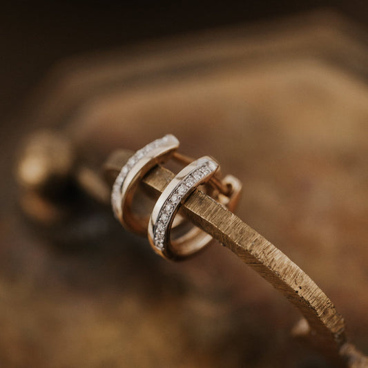 Close-up of gold earrings with diamond accents on a wooden surface.