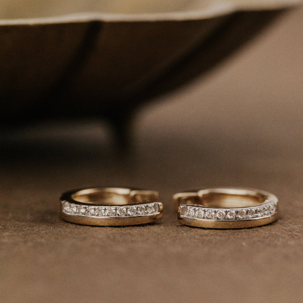 Two gold earrings with diamond accents on a brown surface.
