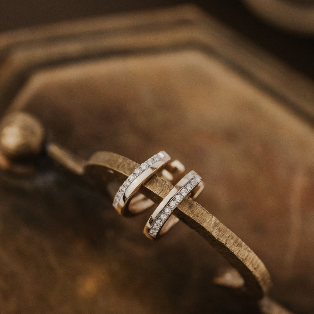 Gold earrings with diamond accents on a textured brown surface.