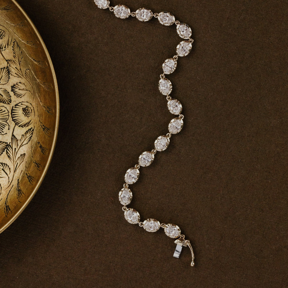 Diamond tennis bracelet on a brown textured surface with an ornate gold dish.