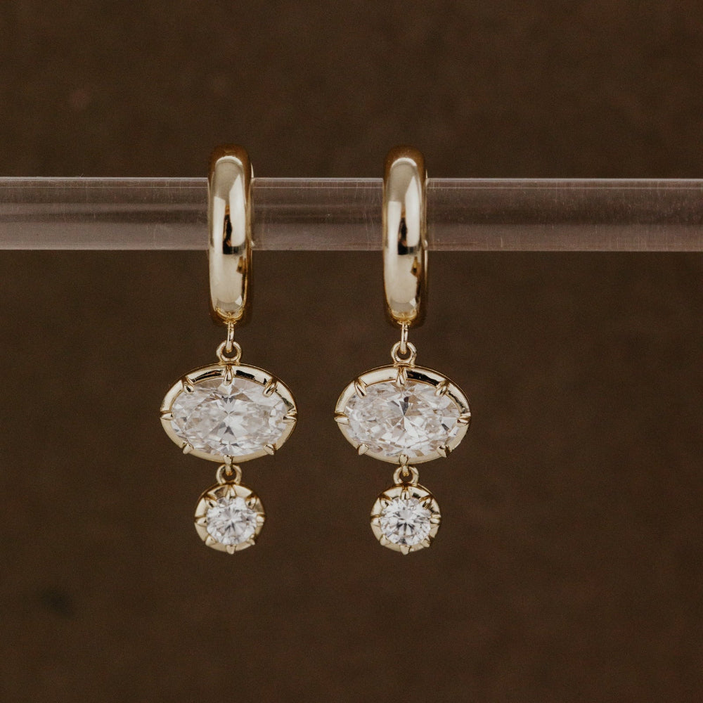 Gold huggie hoop earrings with lab grown diamond dangles on a clear rod against a brown background.