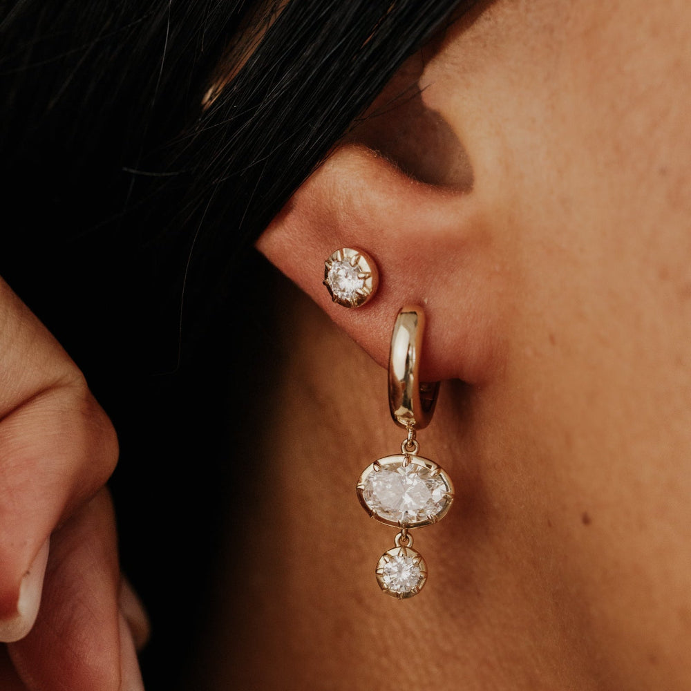 Close-up of an ear wearing gold huggie hoop earrings with lab grown diamond dangles.