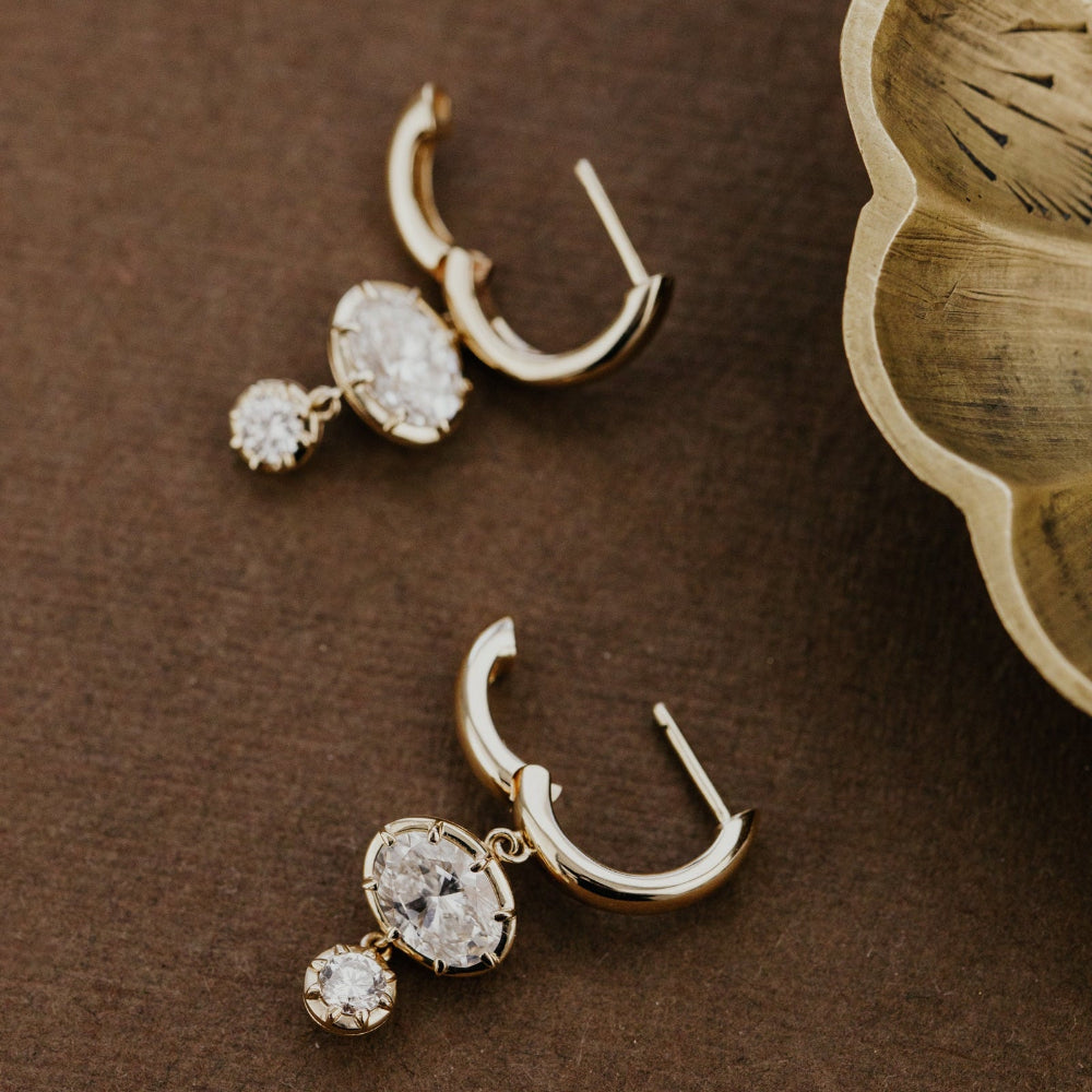 Pair of gold hoop earrings with lab grown diamonds on a brown surface.