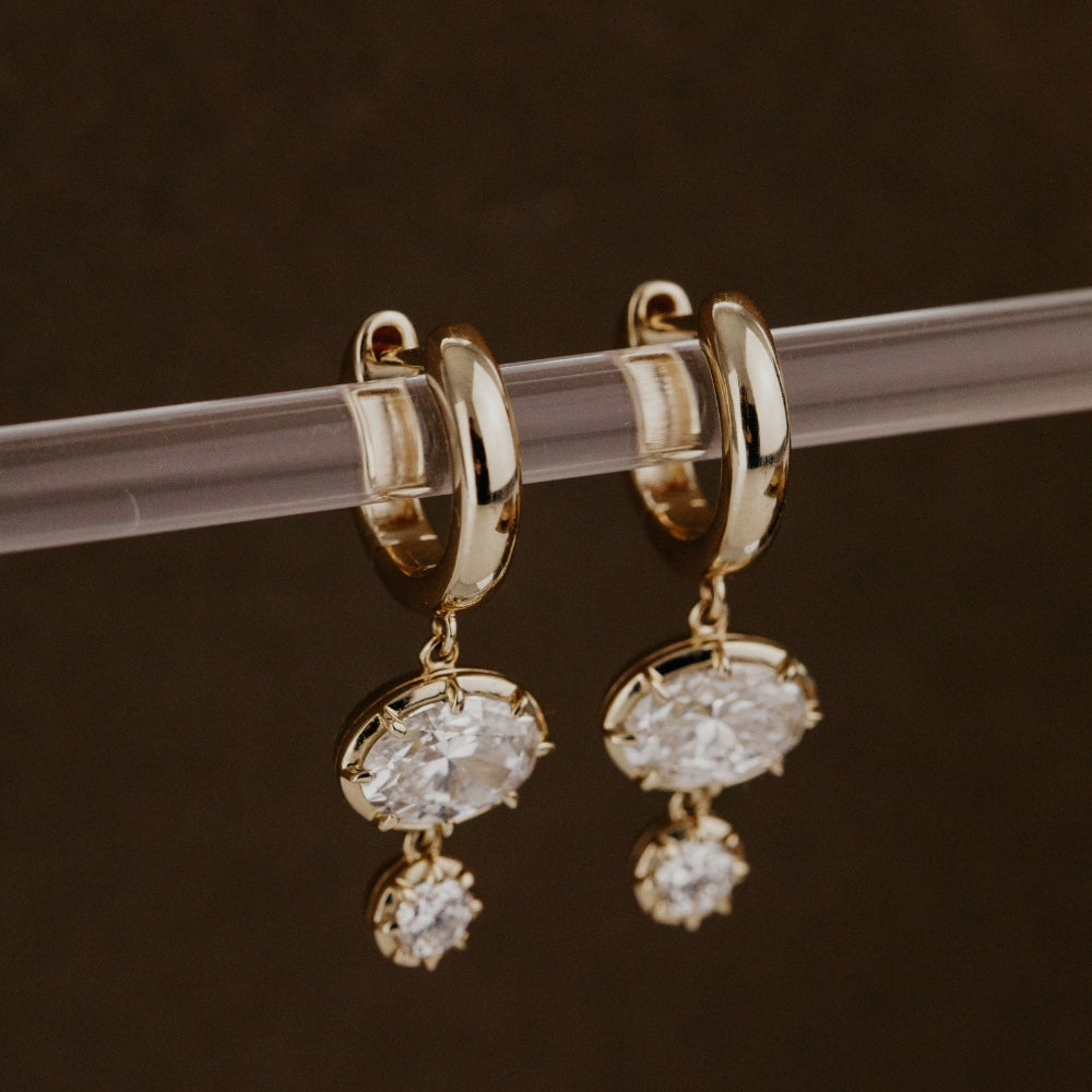 Gold hoop earrings with lab grown diamond dangles on a clear rod against a dark background.