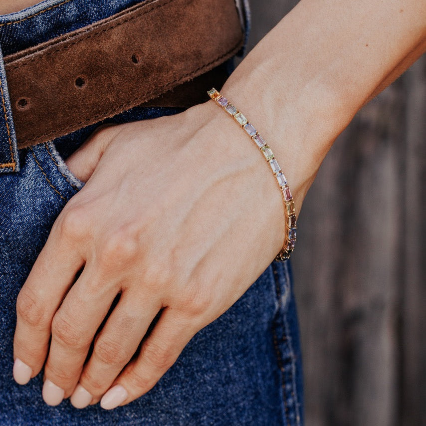 The Pastel Emerald Cut Sapphire Tennis Bracelet in 14k yellow gold worn on the wrist against a casual denim outfit.
