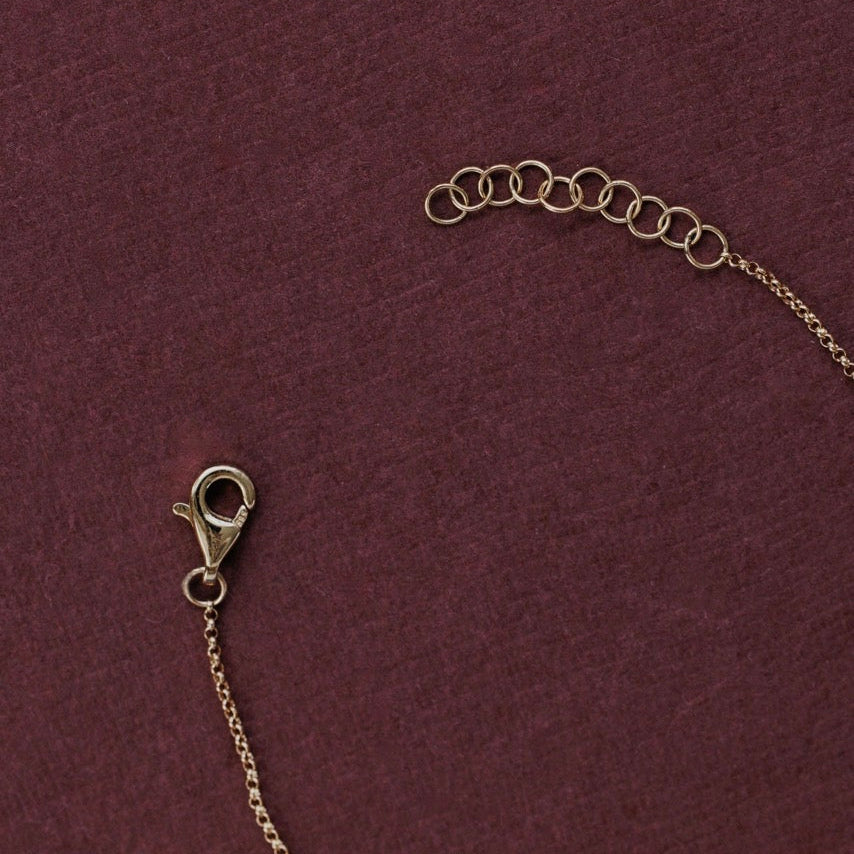 Close-up of a gold-toned chain necklace extender with a lobster clasp and a series of small connecting rings, laid on a textured dark burgundy background.