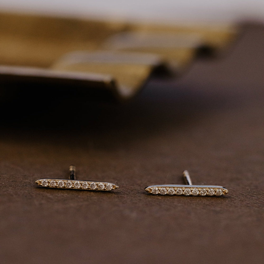 Pair of gold earrings with small diamonds on a brown surface.