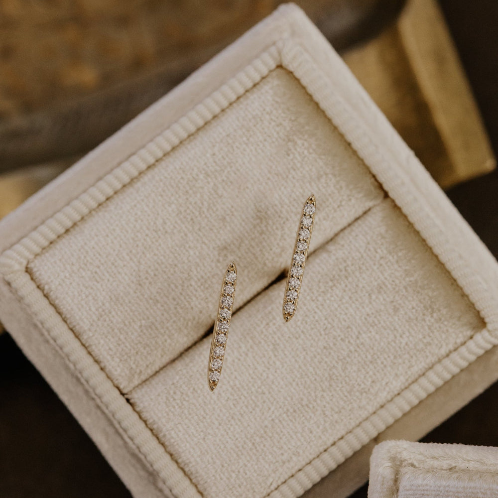 Pair of diamond earrings in a jewelry box on a wooden surface.