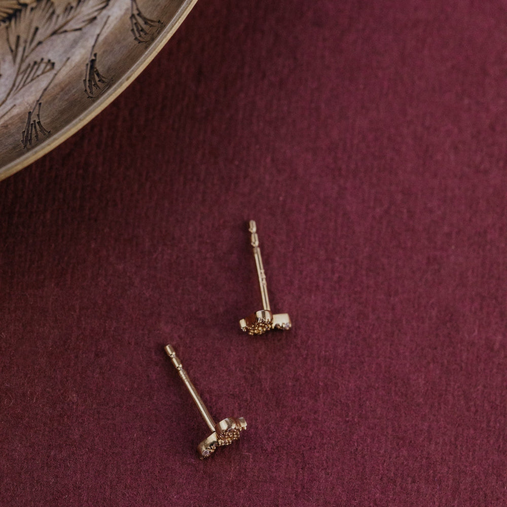 Gold earrings on a maroon fabric background.