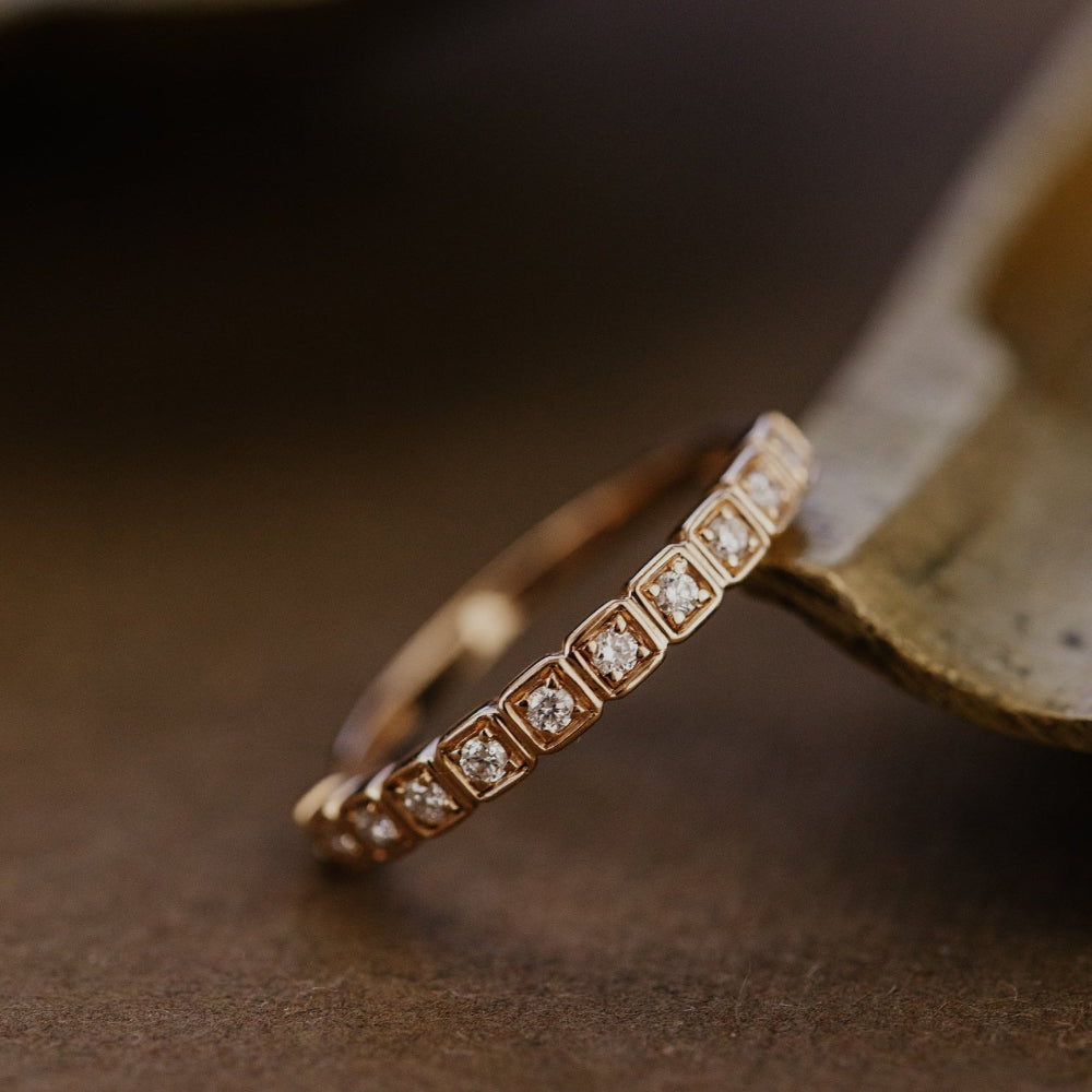 Rose gold wedding band with diamonds on a brown surface.
