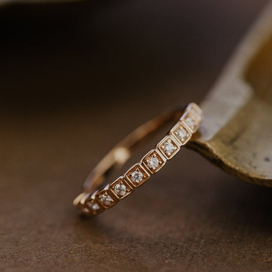 Rose gold wedding band with diamonds on a brown surface.
