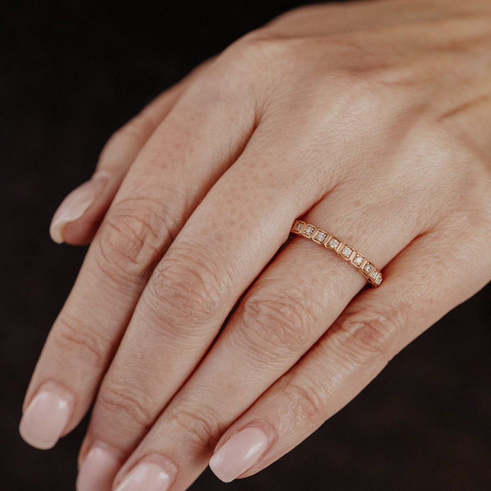 Hand wearing a gold diamond wedding band on a dark background.