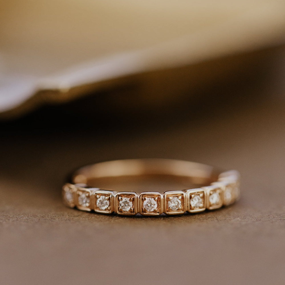 Rose gold wedding band with diamonds on a wooden surface.