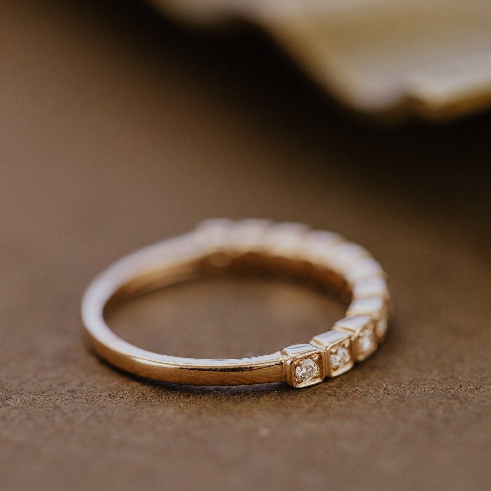 Gold wedding band with small diamonds on a brown surface.