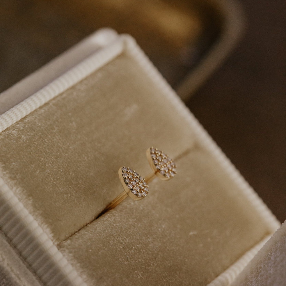 Gold earring with pear-shaped diamond design in a beige jewelry box.