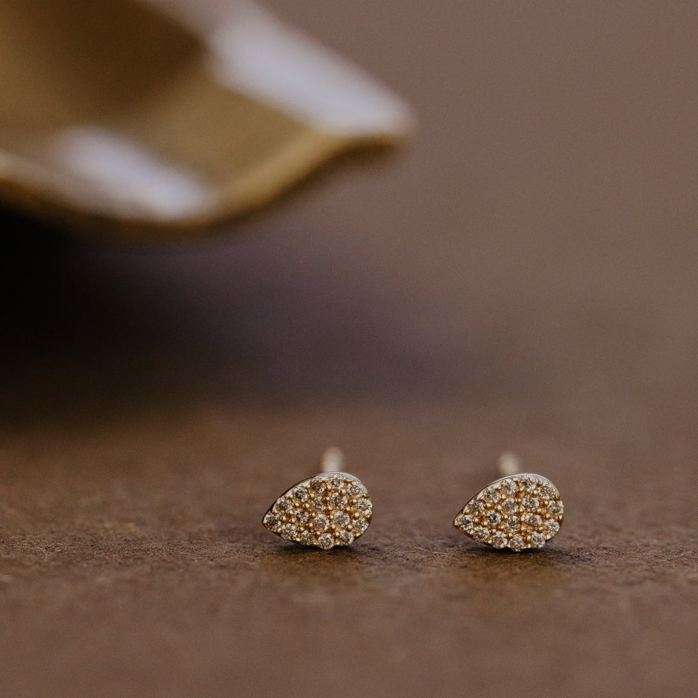 Pair of gold pear-shaped pave diamond earrings on a brown surface.