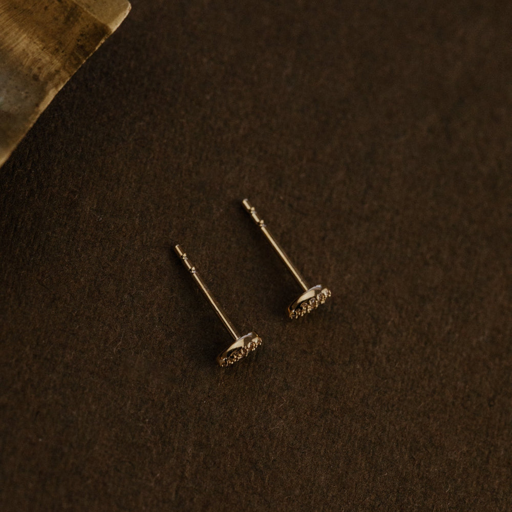 Gold earrings on a dark brown surface.