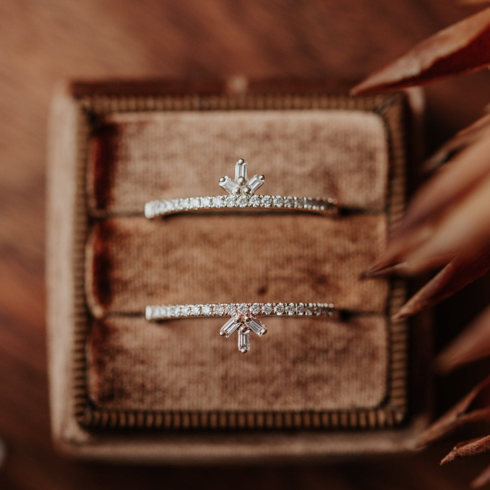 Two gold wedding bands with decorative diamond designs on a textured brown surface.