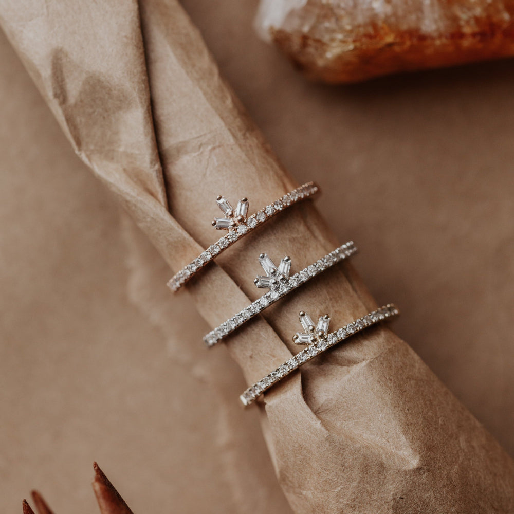 Three diamond wedding bands in different gold colors on a beige napkin with a blurred background.