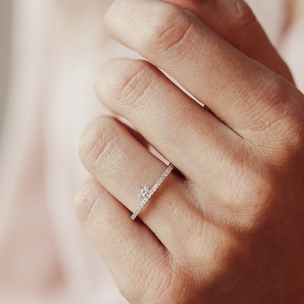 Close-up of a hand wearing a diamond wedding band with a soft background.