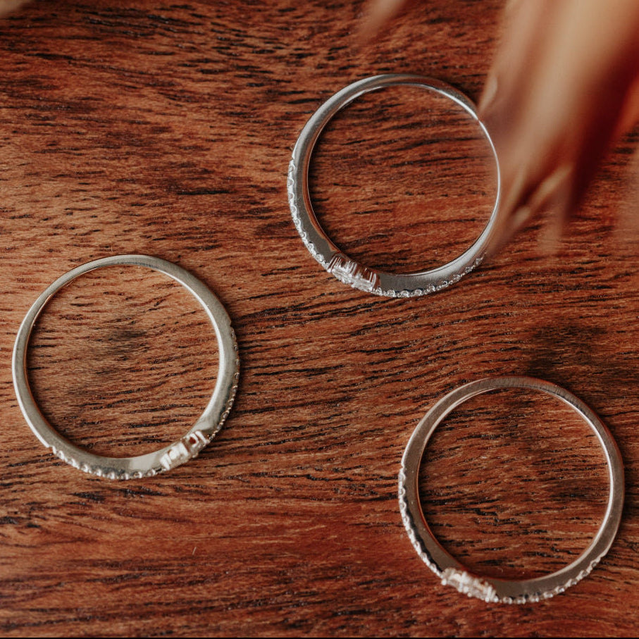 Three gold wedding bands on a wooden surface with dried flowers in the background.