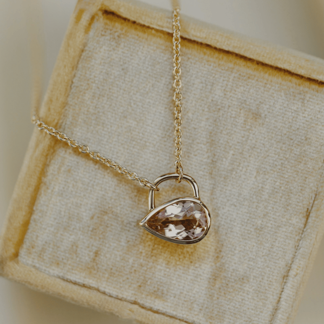 A light pink Pear shaped morganite stone in a bezel setting on a light colored jewelry box. 