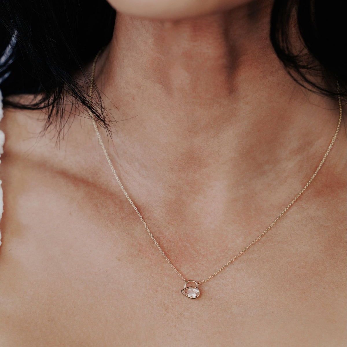 A light pink Pear shaped morganite stone in a bezel setting on the neck of a model 