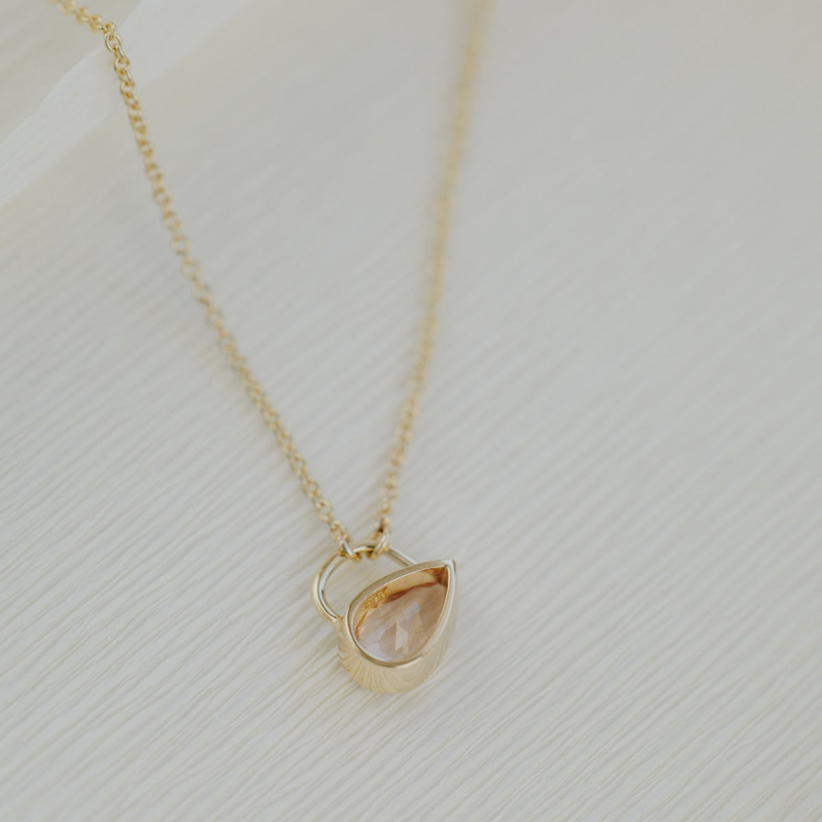 The backside of a light pink Pear shaped morganite stone in a bezel setting on a textured white background.