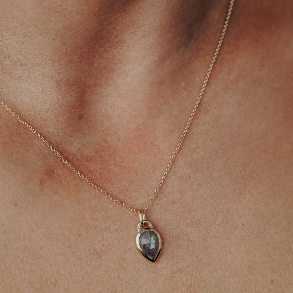 A 14k yellow gold pear shaped labradorite necklace in a bezel setting featured on the neck of a model.