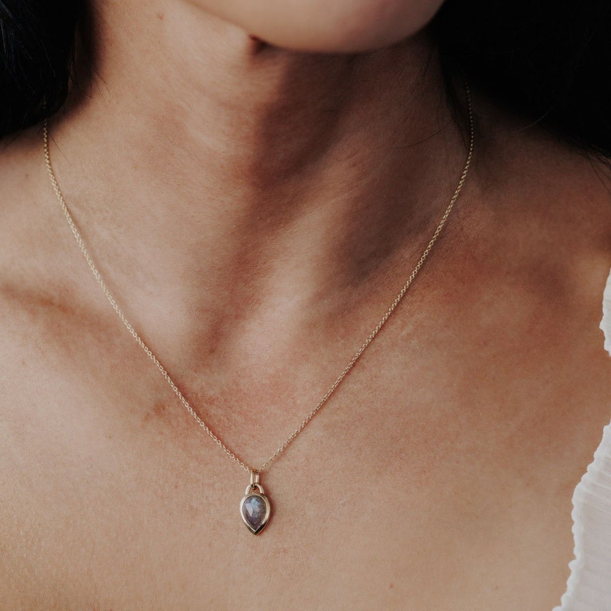 A 14k yellow gold pear shaped labradorite necklace in a bezel setting featured on the neck of a model.