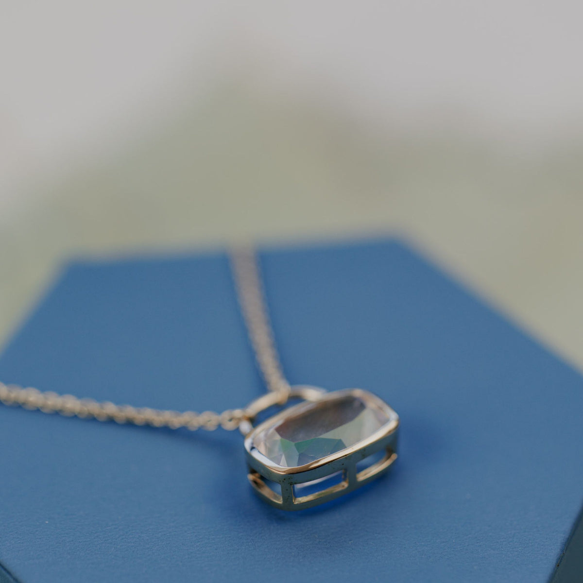 A 14k yellow gold cushion cut moonstone necklace in a bezel setting with a lock style design on blue jewelry box. 