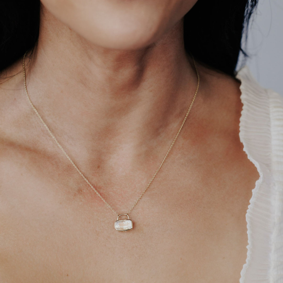 A 14k yellow gold cushion cut moonstone necklace in a bezel setting with a lock style design on the neck of a model.