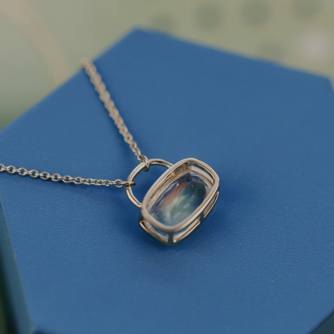 The back side of a 14k yellow gold cushion cut moonstone necklace in a bezel setting with a lock style design on blue jewelry box. 