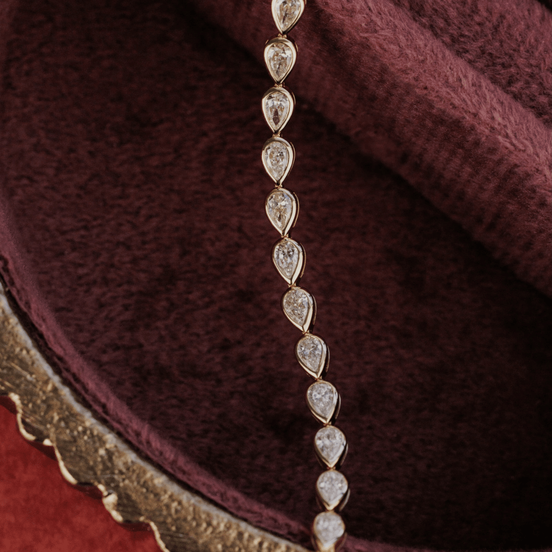 14k gold pear cut, lab grown diamond tennis bracelet featured on a textured red jewelry box. 