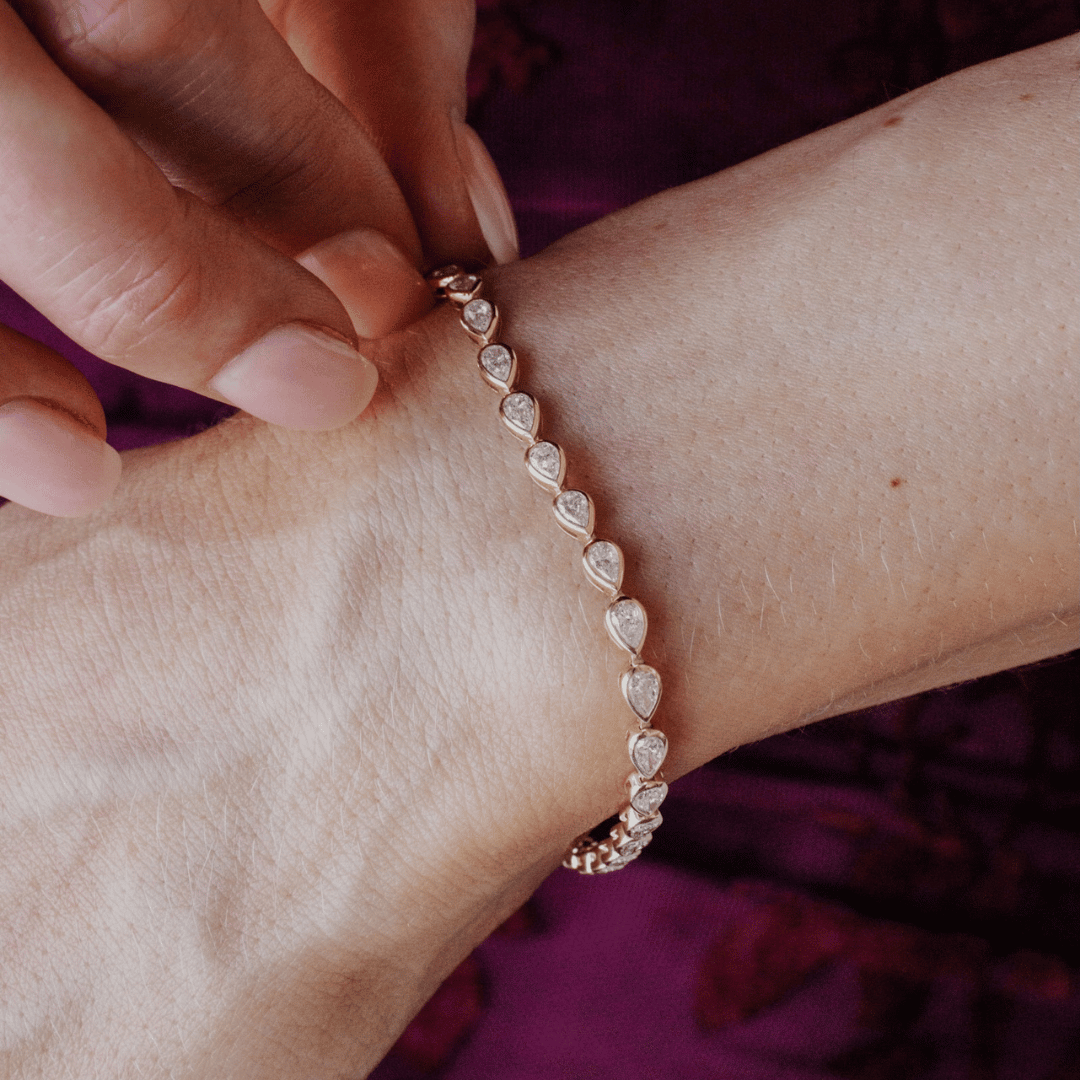 14k gold pear cut, lab grown diamond tennis bracelet featured on the wrist of a model. 