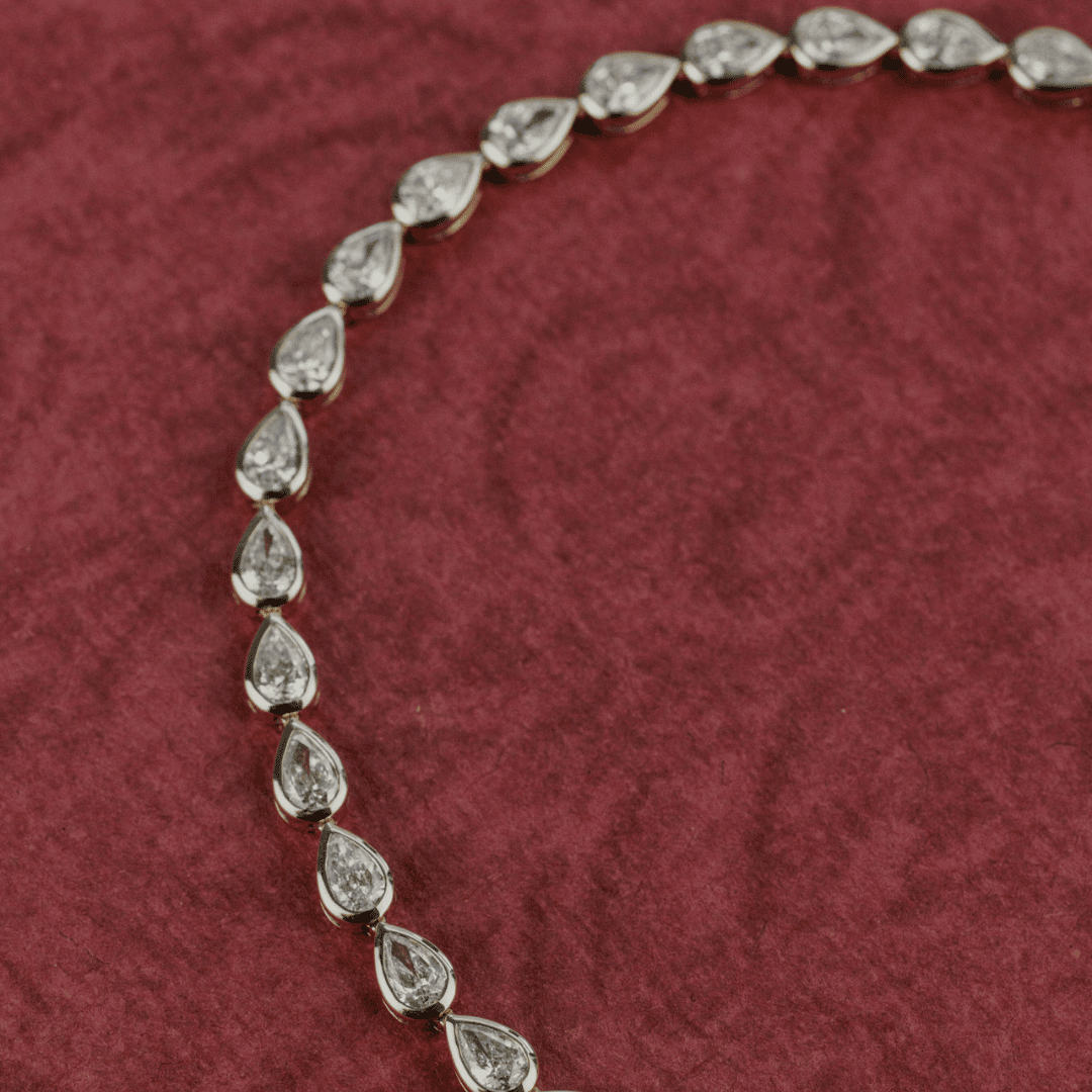 14k gold pear cut, lab grown diamond tennis bracelet featured on a textured red surface.  