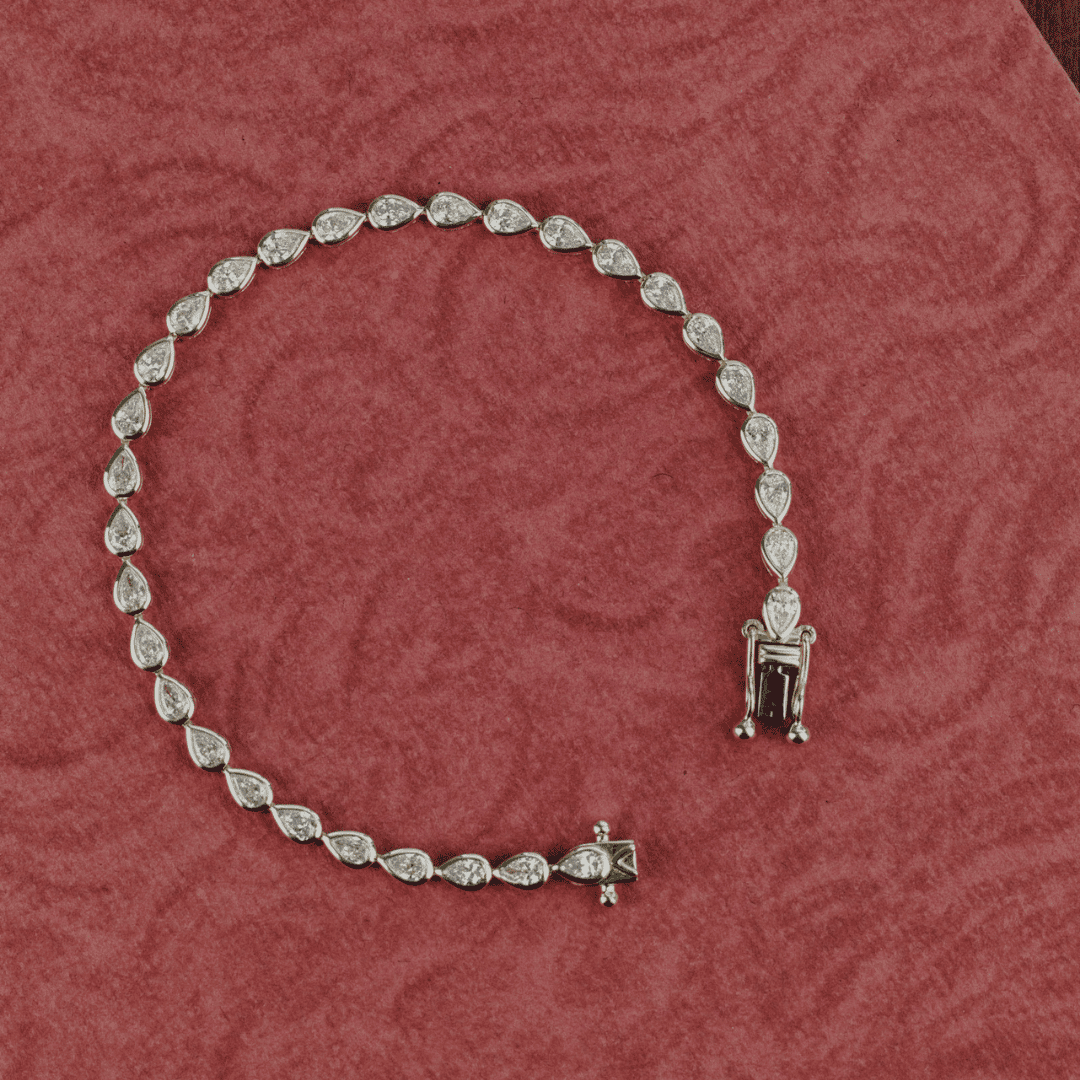 14k gold pear cut, lab grown diamond tennis bracelet featured on a textured red surface.  
